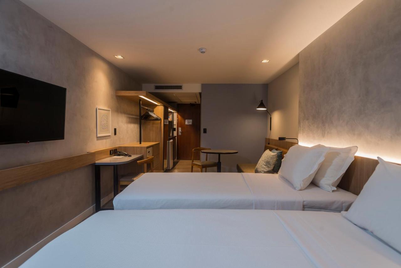 Hotel Luzeiros Fortaleza Exterior foto The photo shows a hotel room with a modern and minimalist design. There are two single beds with white linens and pillows placed next to each other. A wall-mounted flat-screen TV is positioned above a small table or desk area, which has a wooden fini