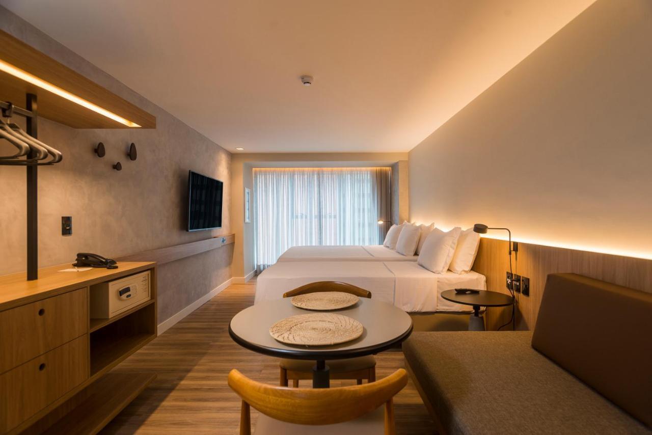 Hotel Luzeiros Fortaleza Exterior foto The photo shows a modern hotel room with a clean and minimalist design. It features two beds with white bedding positioned against a wall. There is a large window with sheer curtains allowing natural light to fill the space. Opposite the beds, a flat