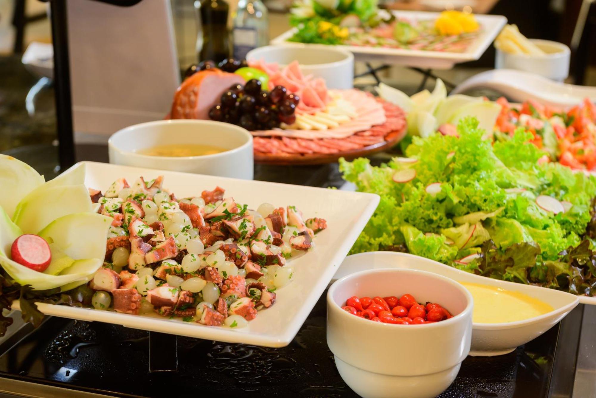 Hotel Luzeiros Fortaleza Exterior foto The photo shows a variety of food items arranged on a table. In the foreground, there is a white plate with a mixed dish that includes chopped ingredients, likely vegetables and possibly meat, garnished with herbs. Surrounding this dish are several b